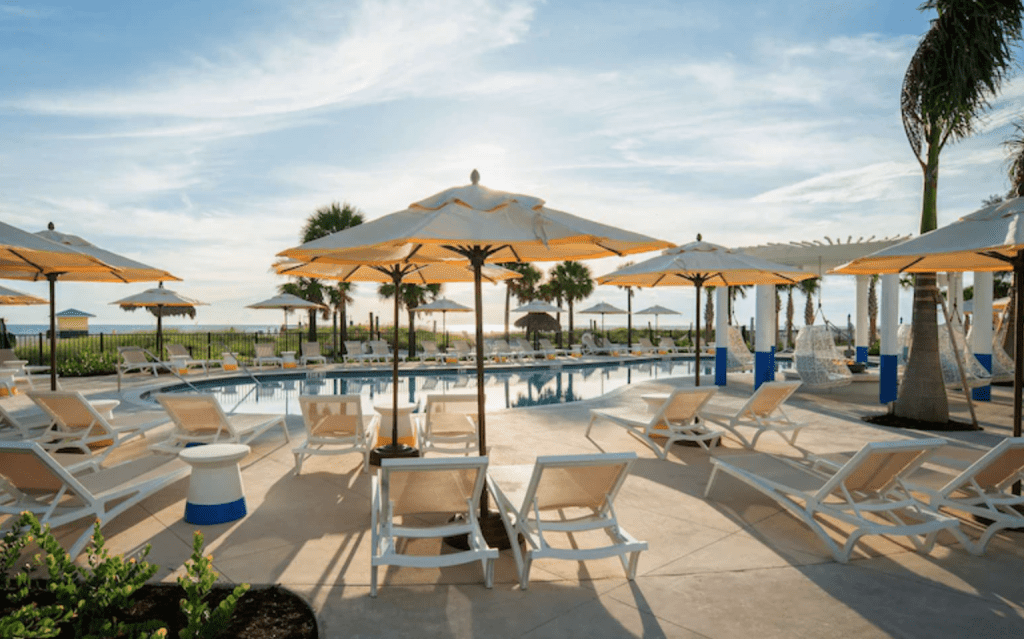 Light colored umbrellas stand over lounge chairs around a pool at an Sirata Beach Resort, an all-inclusive resort perfect for weekend getaways in Florida.