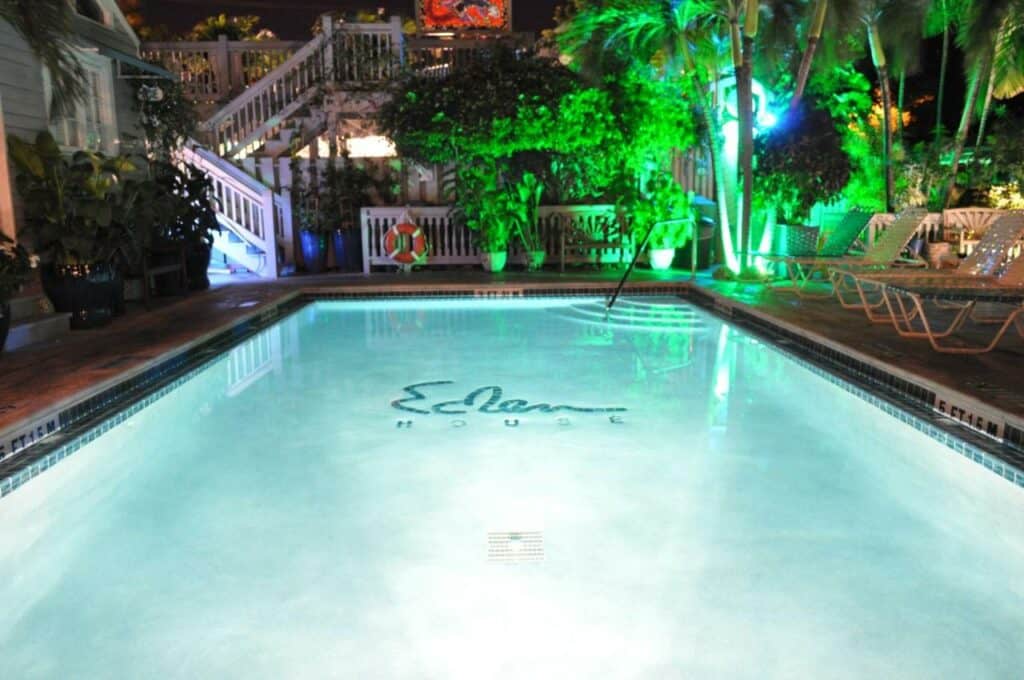 A shot of a lit pool at night, the water glows a bright blue, and the logo of the hotel is on the bottom of the pool. The pool area is lit with colorful lights and is surrounded by lush greenery one of the best boutique hotels in florida