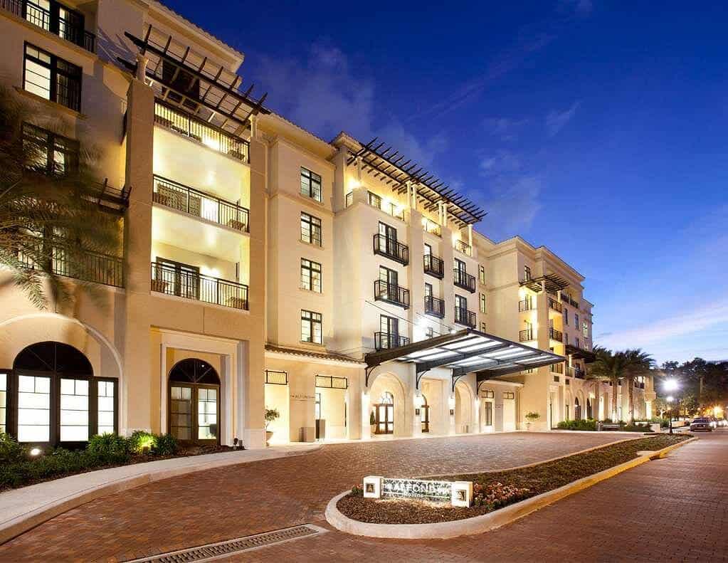 A morning shot of the Alfond Inn's exterior, which is a classic white stucco with black trimming and railings. The sun is just rising in the background washing everything in a cool morning light 