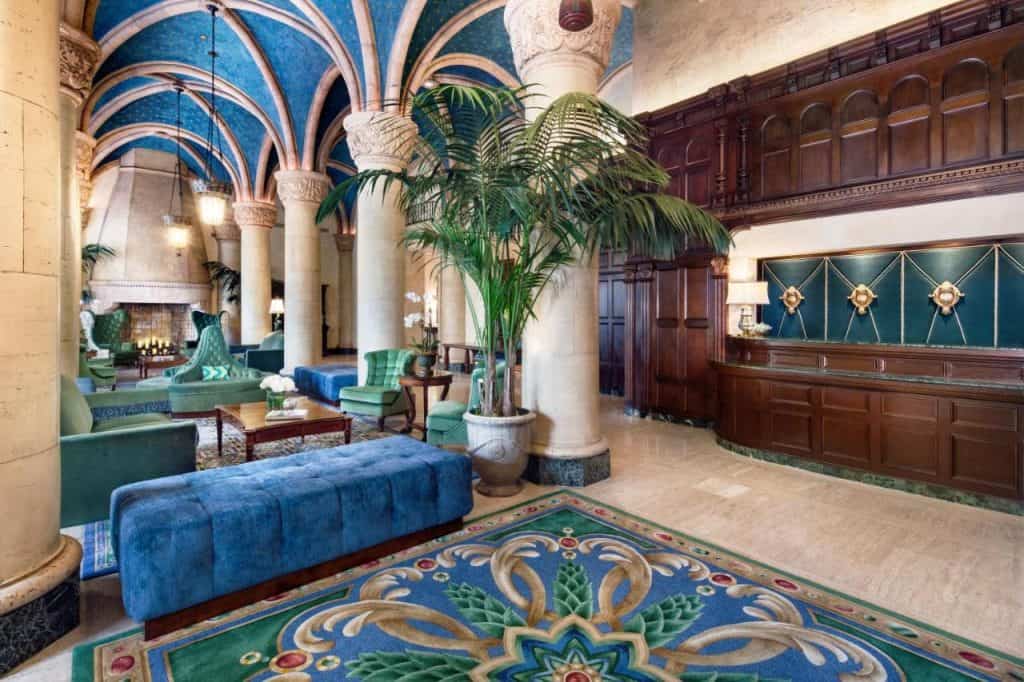 A shot of a sitting area in the Biltmore - the room has large ornately designed rugs and lots of plush blue and teal furniture. The ceilings are arched and have gorgeous blue tiles decorating wide swaths of it