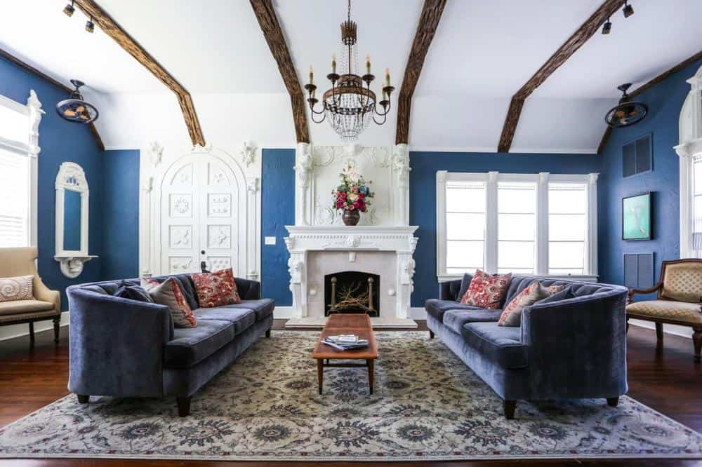 A shot of a sitting area in Kenwood gables, the rectangular room has blue walls, the sofas are dark purple and the fireplace in the center is all-white which makes for a stunning contrast against the darker colors in the room