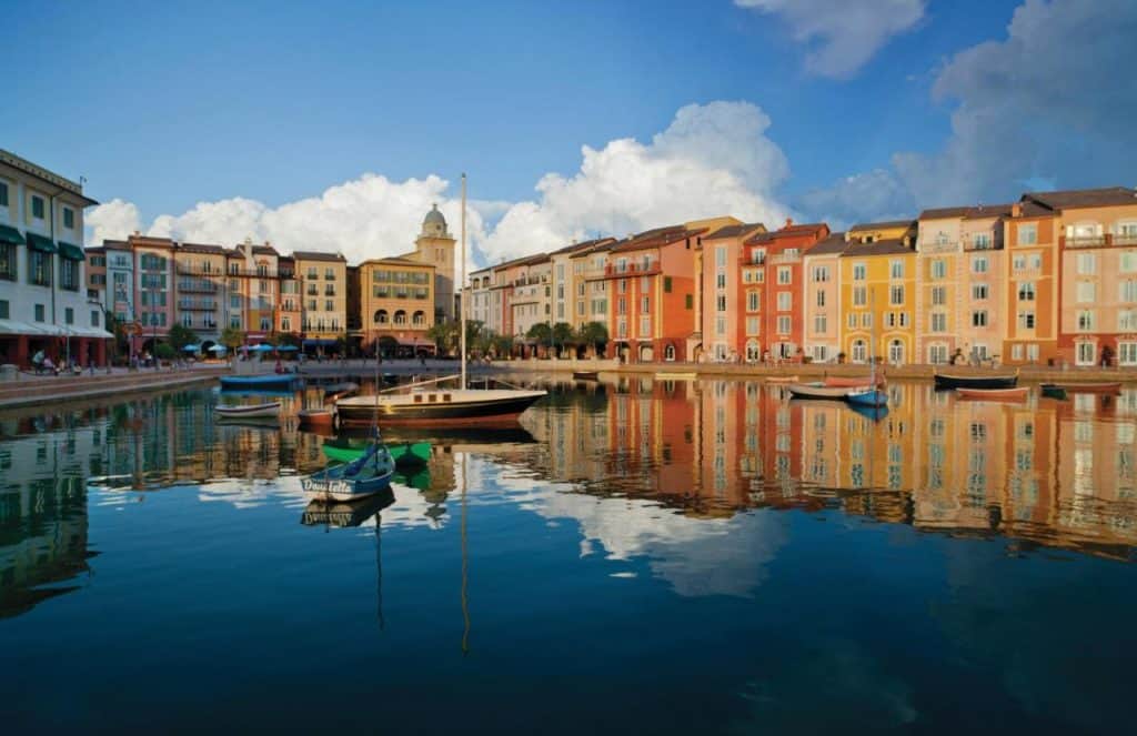 A shot of the Loews Portofino Hotel, the water is in the foreground with the bright fall colors of the hotel's buildings in th ebackground. There are a few boats in the water which is beautifully reflective and calm