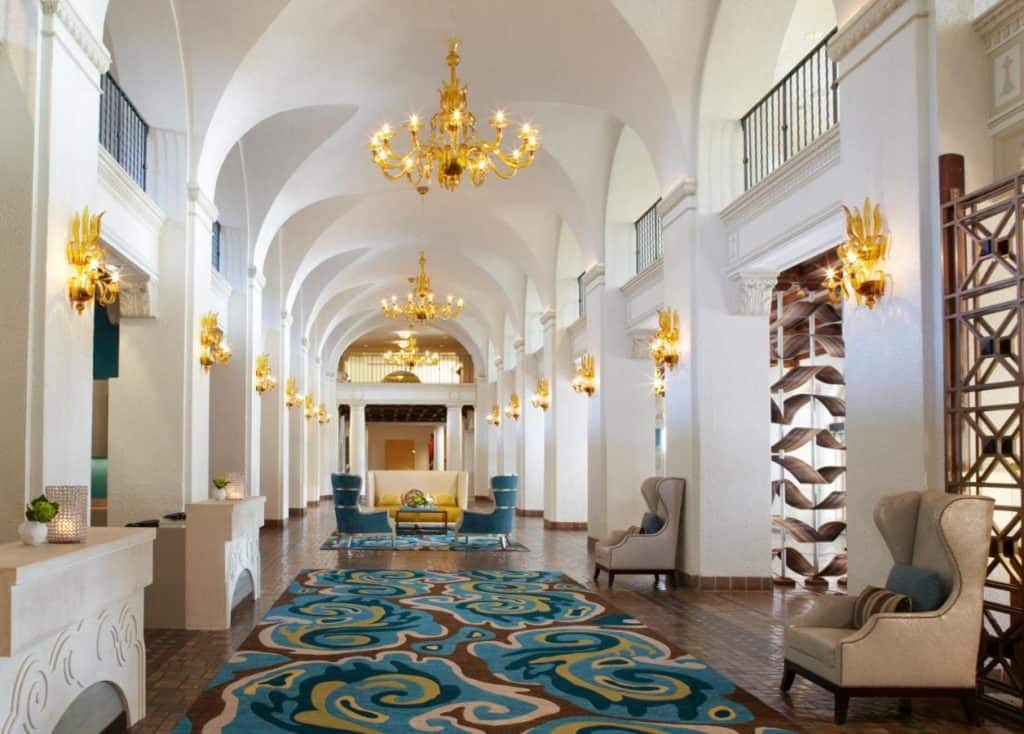 The reception room of the the vinoy hotel, the ceilings are arched above white walls, with bright golden light fixtures, the hallway is long and filled with blue, green, and brown furnishings 