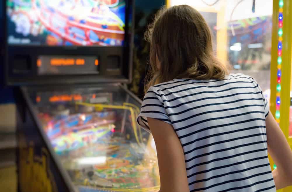 A person in a white and black stripped shirt playing on a pinball machine. 