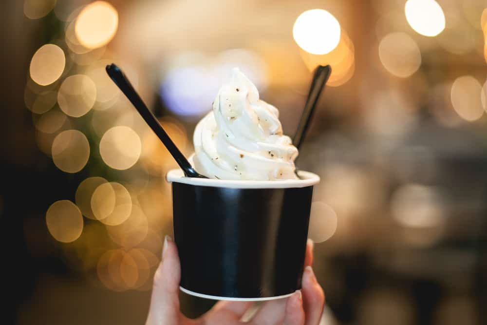 A cup of soft serve ice cream is held in a person's hand as they raise it up to the lights at one of the restaurants in Punta Gorda: the cup has two spoons in it.