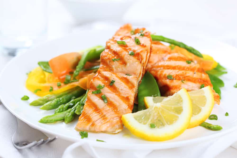 Plate of salmon on a bed of vegetables with lemon slices.