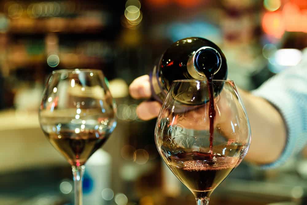 A person pouring red wine into a glass.