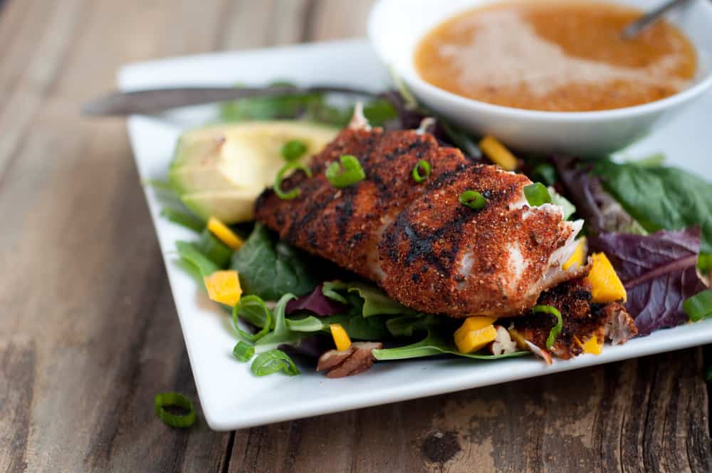 Blackened Fish on a plate with some salad and a side of dipping sauce. 