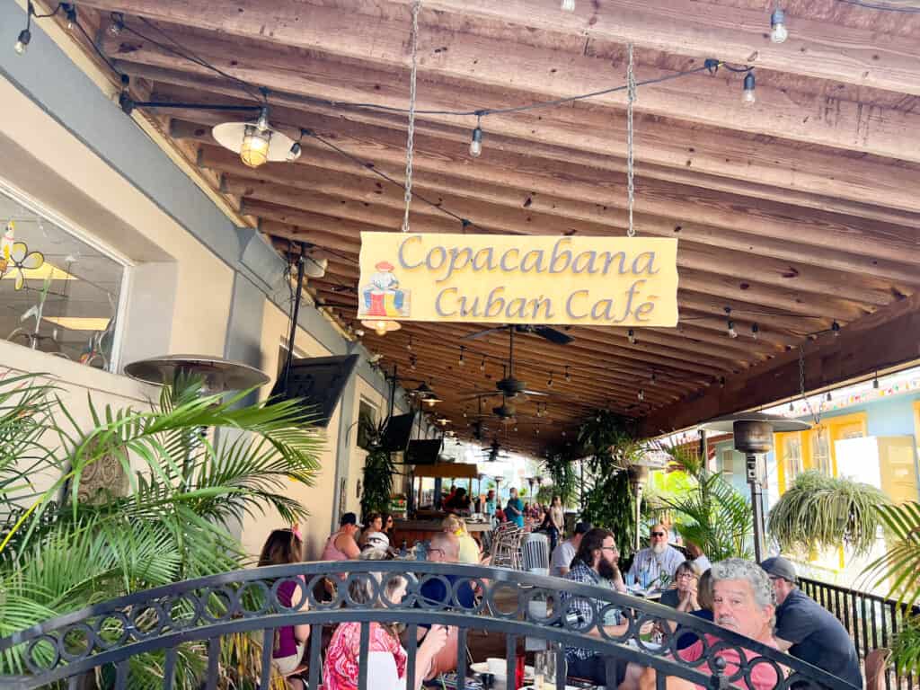 The patio of The Cuban Cafe in Mount Dora. Peaople are sat at tables under a covered wood roof.   