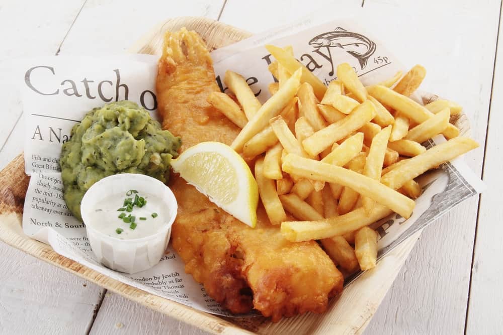 Fish and chips in a basket lined with newspaper. There is a lemon on top a side of musuhy peas and some sauce. The artcle is about restaurants in Mount Dora 