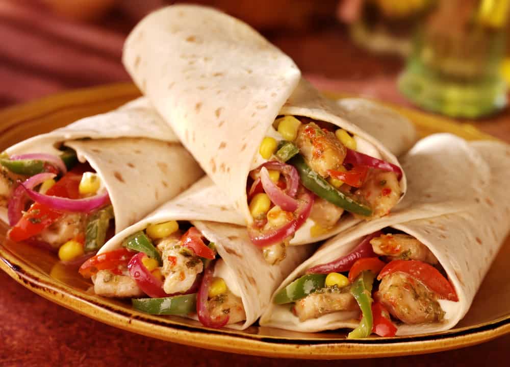 4 rolled fajitias on a plate. They contain chicken, sweetcorn, peppers and onions.  