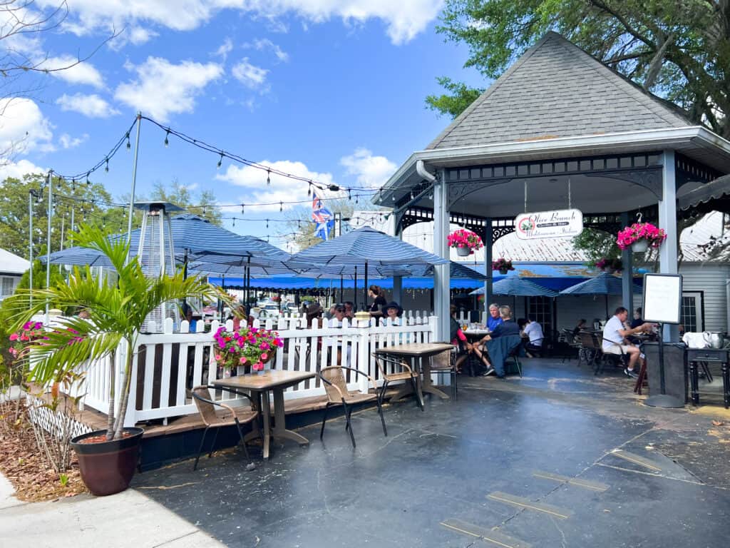 The Olive Branch restaurant. There are tables and chairs outside surrounded by a white fence.   