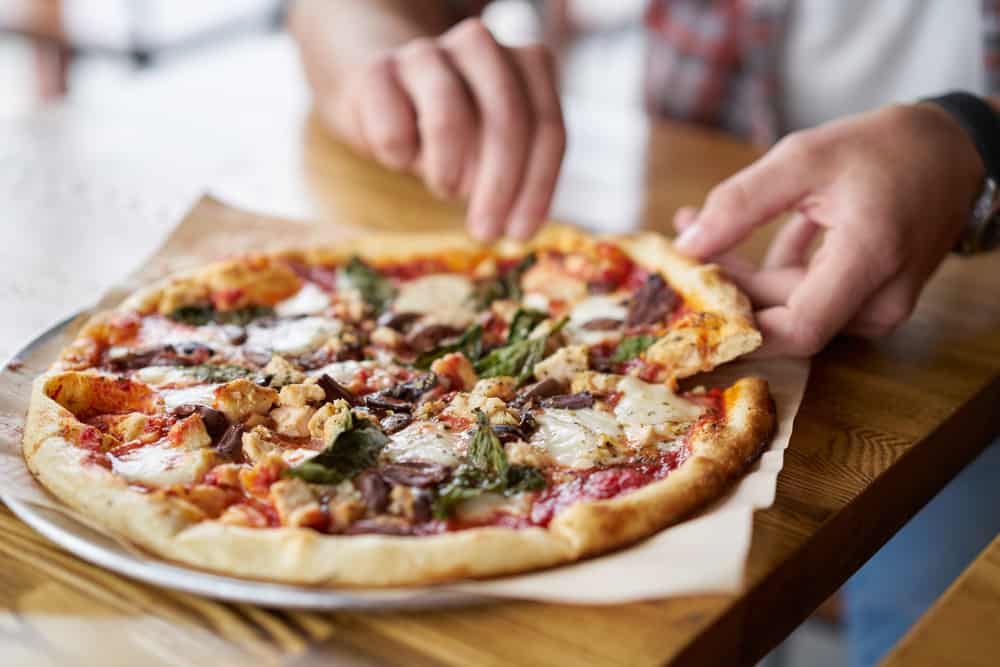 A man taking a slice of pizza from a plate on a table. 