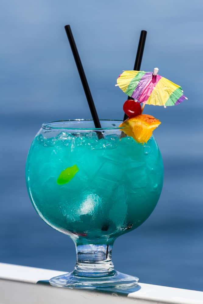 The fish bowl drink is popular at one of the best restaurants in Daytona Beach: Sloppy Joes. Drinks like these are massive, in big cups, and are typically full of large amounts of liquor and can be shared: this one is blue in color, as an umbrella, two straws, and sits on a bench by the ocean.