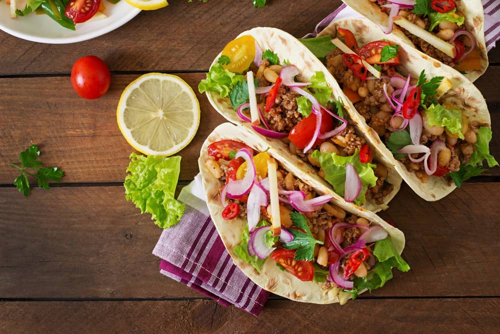 Four tacos sit stuffed in soft shells on a striped blanket, showing off their meat and toppings, like they do at Tia's Tacos, one of the best restaurants in Daytona Beach.