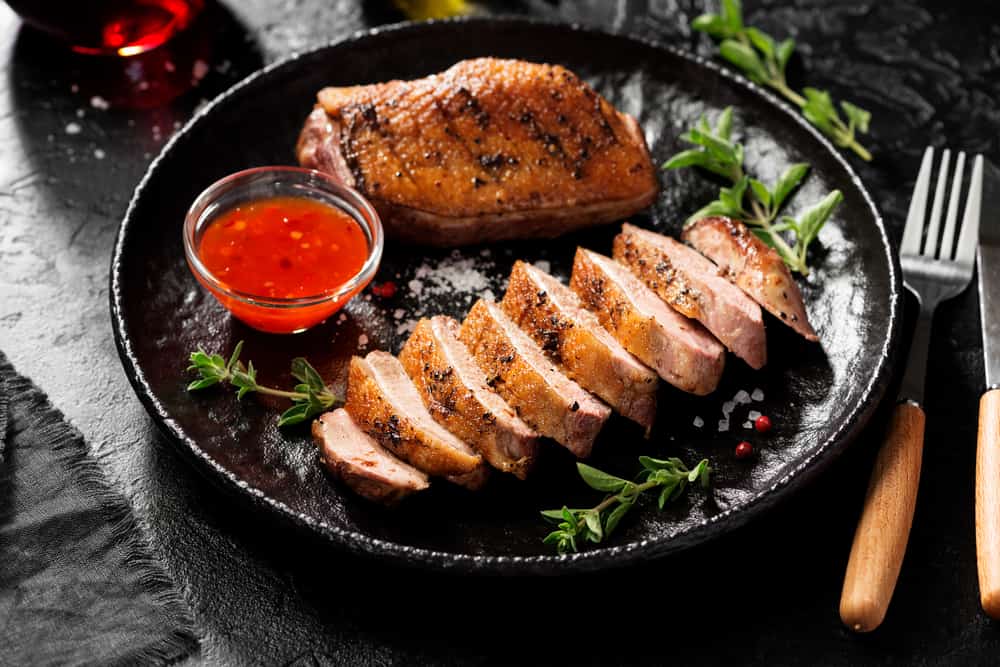 Maple leaf farms duck breast sits cut up on a black plate with dressing and basil on the side: this is a dish you can order at Cielo, one of those nice restaurants in Sanibel! 