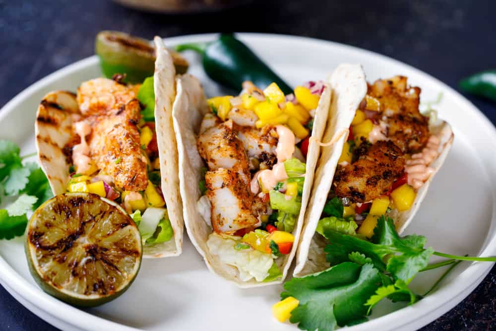 Three fish tacks line up on a white plate at one of the best restaurants in Sanibel. The grilled Mahi is perfectly cooked and topped with mango salsa! 