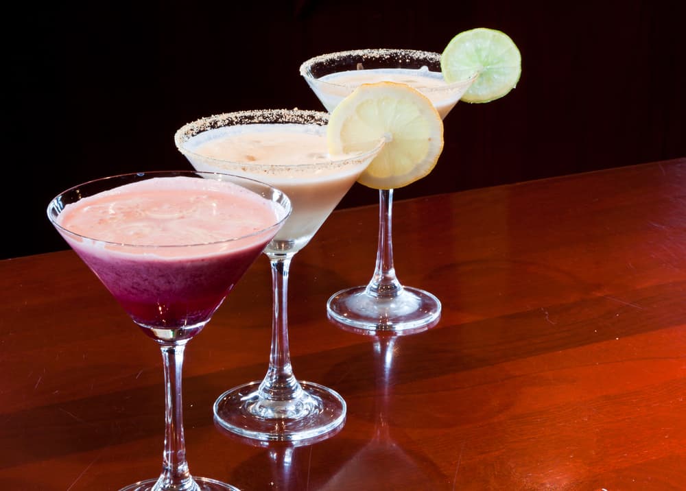 Three cocktails are lined up on a wooden bar, all different colors: pink, orange, and green. The last one is a key-lime pie martini, which is famous at one of the iconic restaurants in Sanibel
