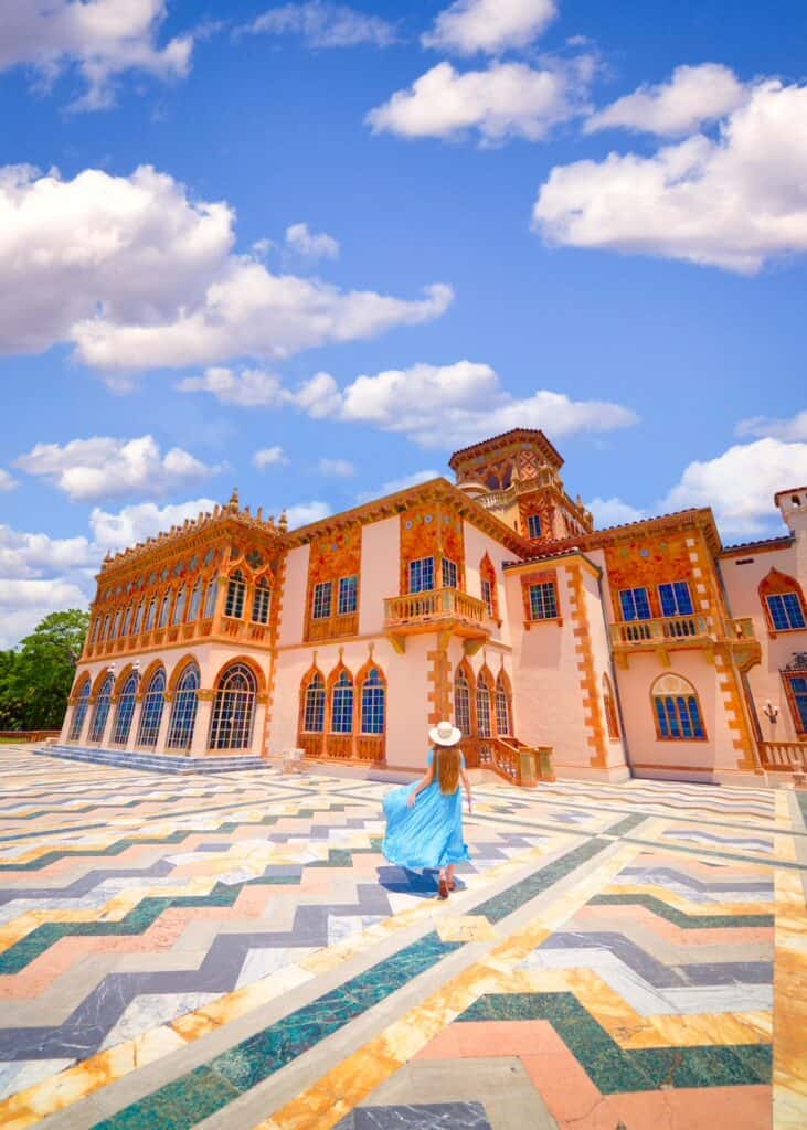 A woman standing in front of the Ringling museum in Sarasota wearing a blue dress.