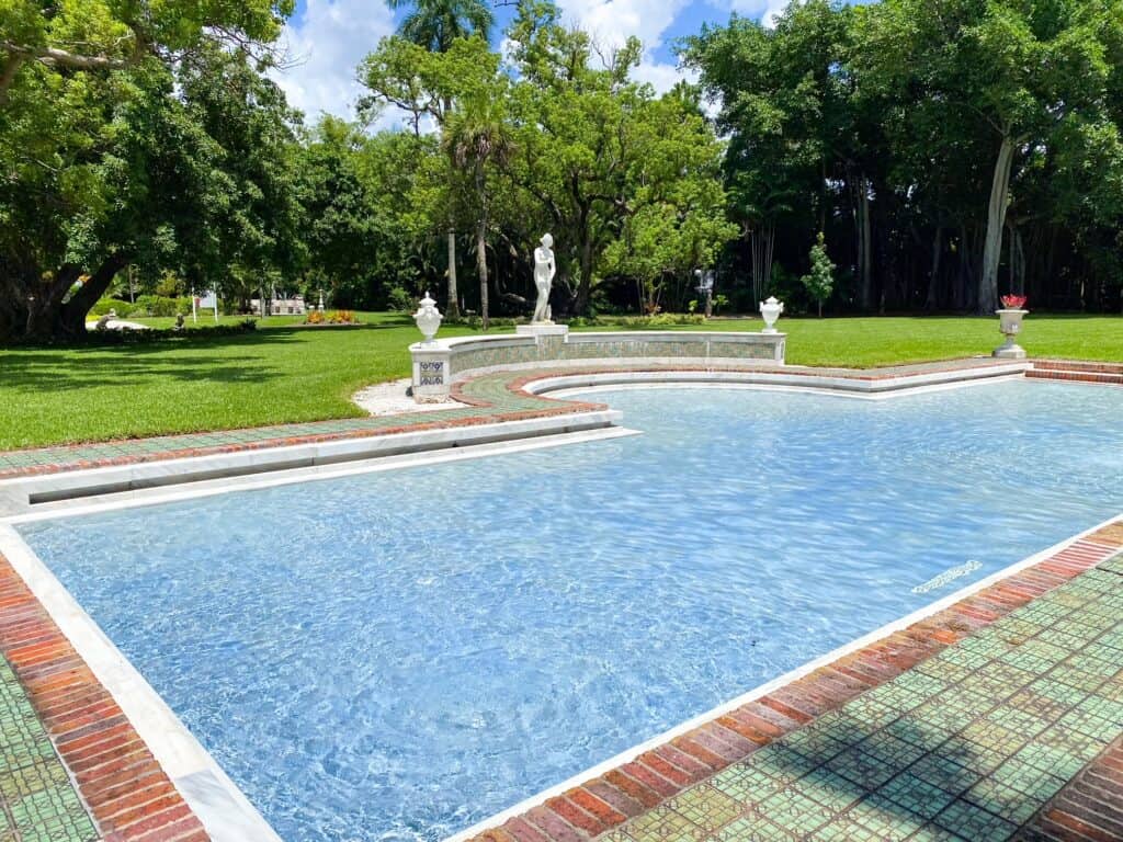 A fountain is blue and bright in the greenery of a garden at the Ringling Museum. 