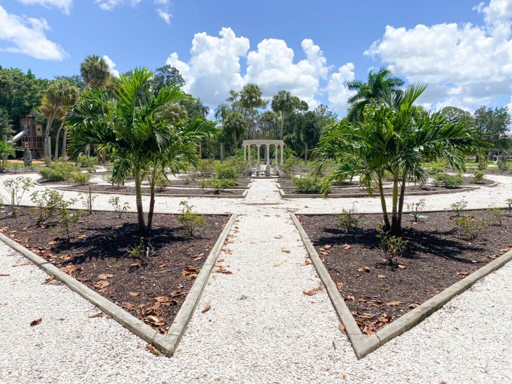 The pathways of the rose garden all lead to a gazebo in the middle, while trees and flowers bloom around it, at the Ringling Museum.