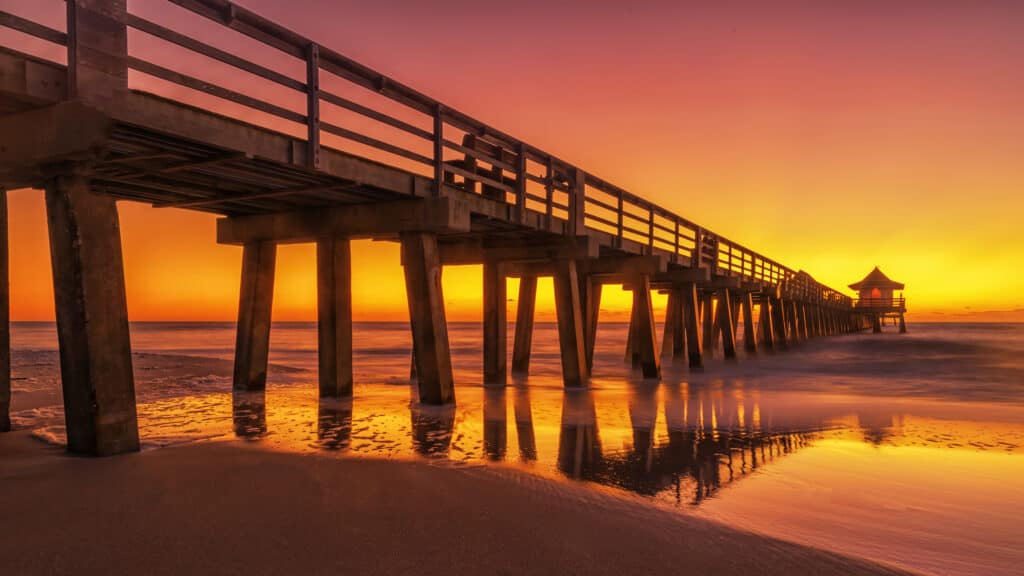 A sunset photo of the naples pier with a glowing orange and red sky