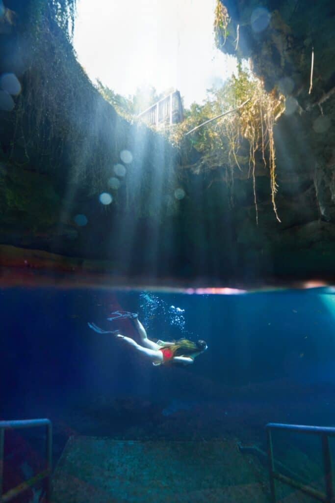 A woman in snorkel gear swims underwater in the Devil's Den cave.