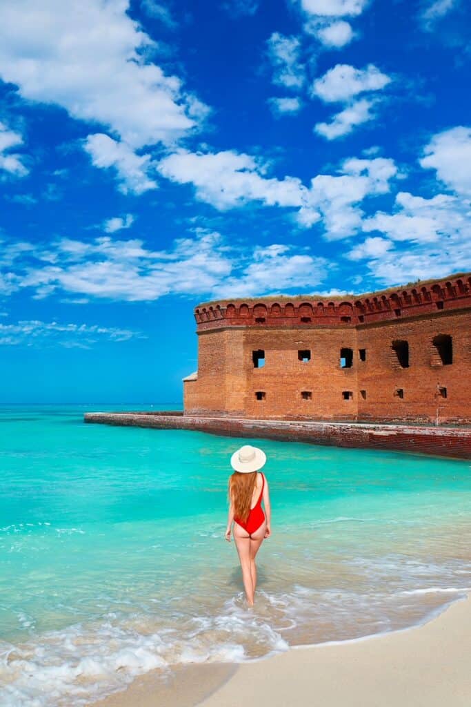 A woman in red swim suit and sun hat stands in the tide in front of the fort on Dry Tortugas, one of the best things to do in Florida.