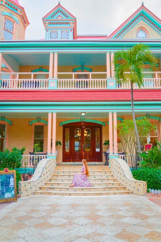 A woman in a floral dress sits on the steps of a colorful house on Duval Street in Key West.