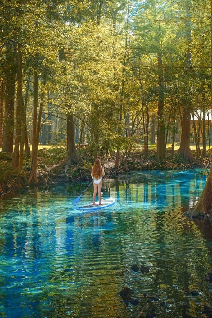A woman with long hair uses a stand up paddle board in Ginnie Springs, one of the best things to do in Florida.