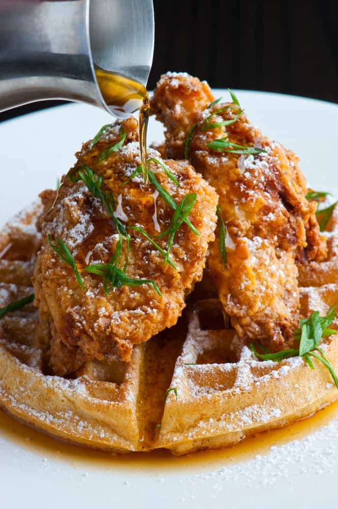 A plate of chicken and waffles with syrup poured on.