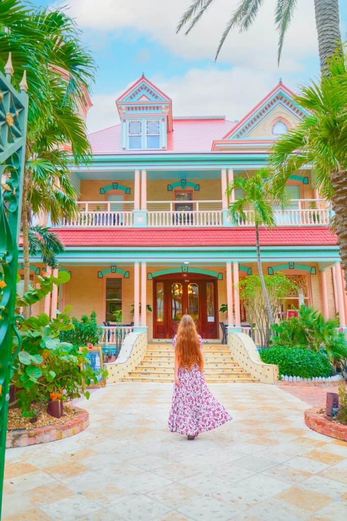 Girl with long hair and a floral dress walks toward a colorful, pastel building.