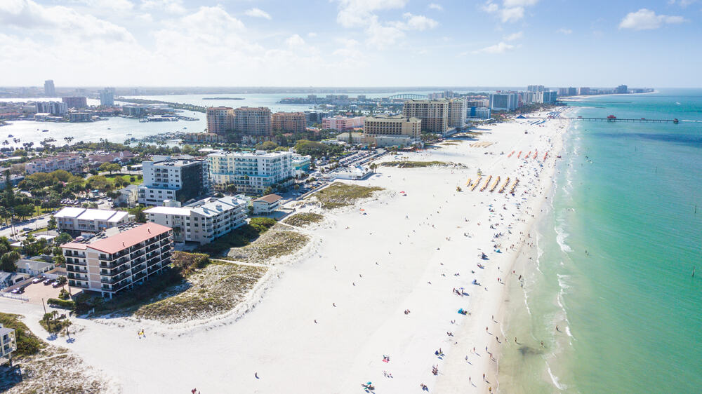 An aerial view of Clearwater Beach, FL with white sand, bright blue water, and building lined up along the beach. The best things to do in Clearwater Beach involve being outside.