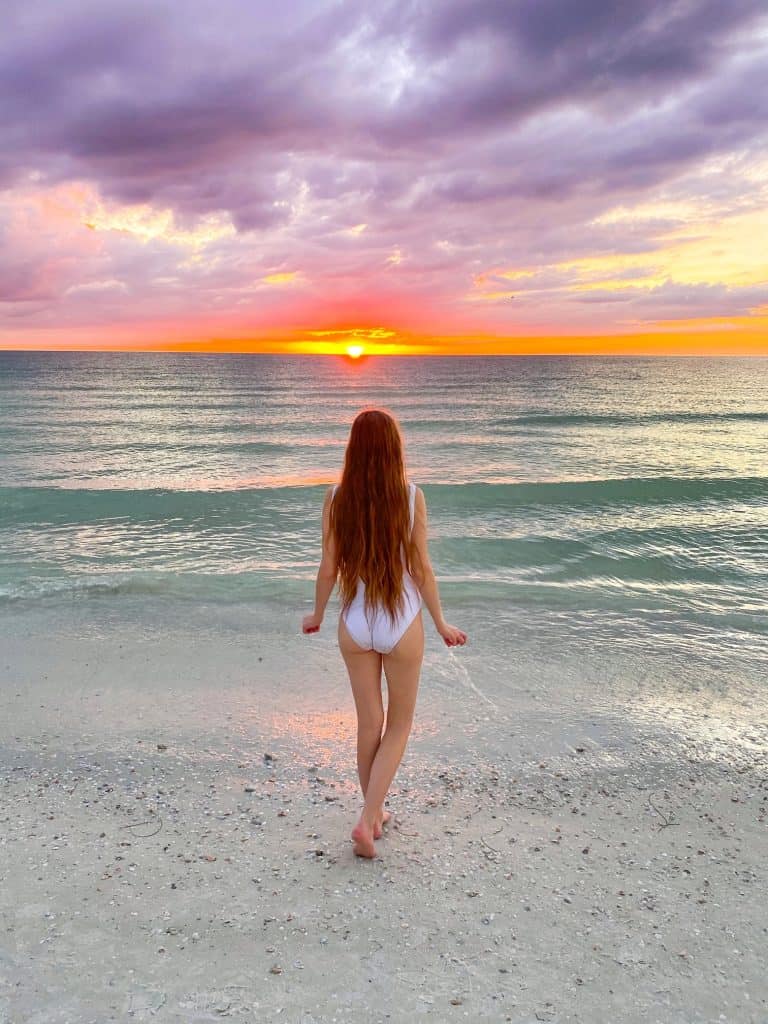 A woman with long hair walks towards the waves, where the sun is setting across Honeymoon Island, one of the best places to visit near Clearwater Beach.