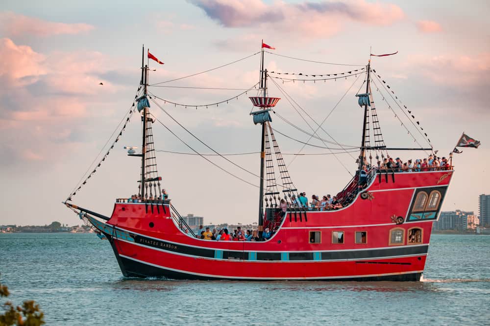 The red and black pirate ship of Captain Memo's Pirate Cruise sets sail, with flags flying from three masts. This pirate cruise is one of the most popular things to do in Clearwater Beach. 