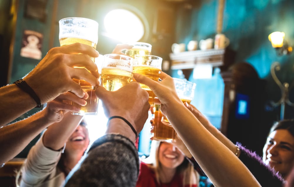 A group of friends lift their beer glasses to the air in a sort of "cheer" at one of the bars in Gainesville.