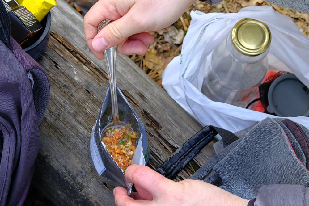 A person spoons out bites of a freeze dried meal while outside. These ready to eat meals are important to avoid hunger, and should be added to your hurricane preparedness list. 