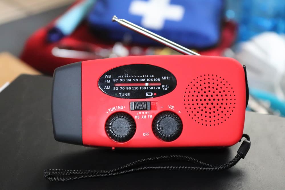 An emergency weather radio, red in color, sits on a table. Having these updates via a radio is perfect for your hurricane preparedness list. 
