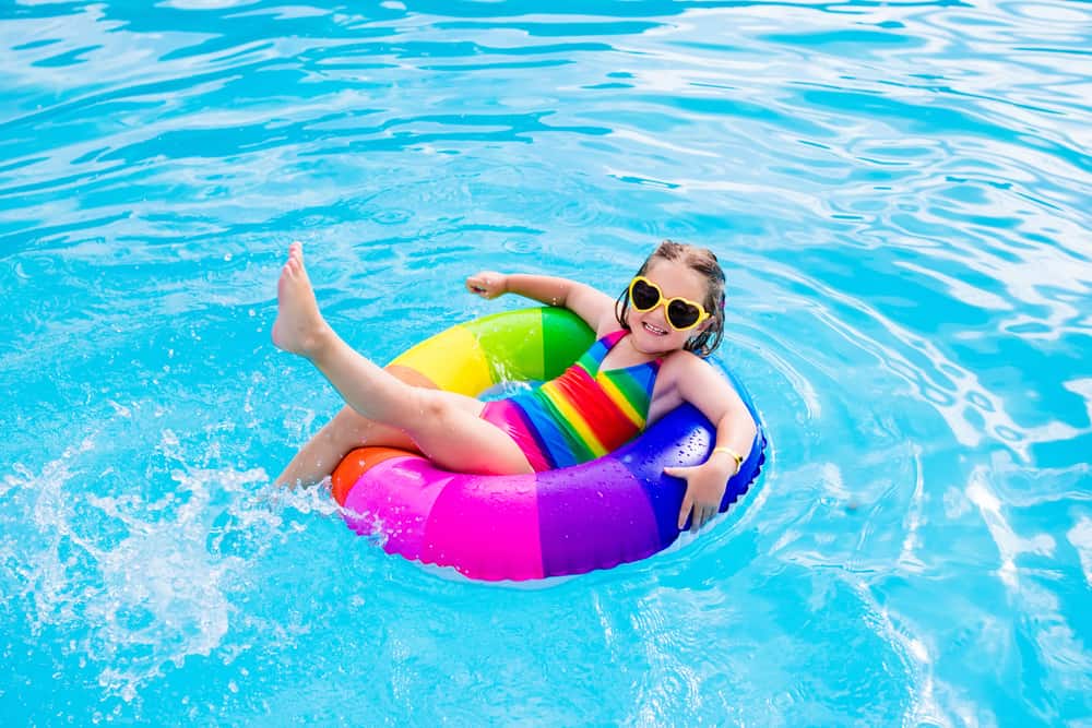 A young girl in a rainbow pool tube in the water.