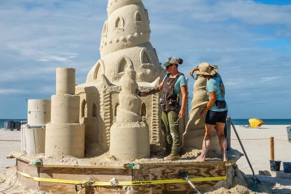 Two sand sculptures work on a large sand castle during the Sanding Ovations competition, one of the best things to do in Treasure Island, FL.