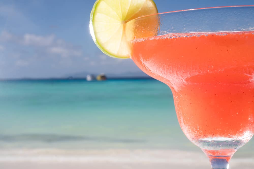 A closeup of a strawberry daiquiri with blue ocean waves in the background, a view similar to that of Caddy's Waterfront restaurant in Treasure Island, FL.