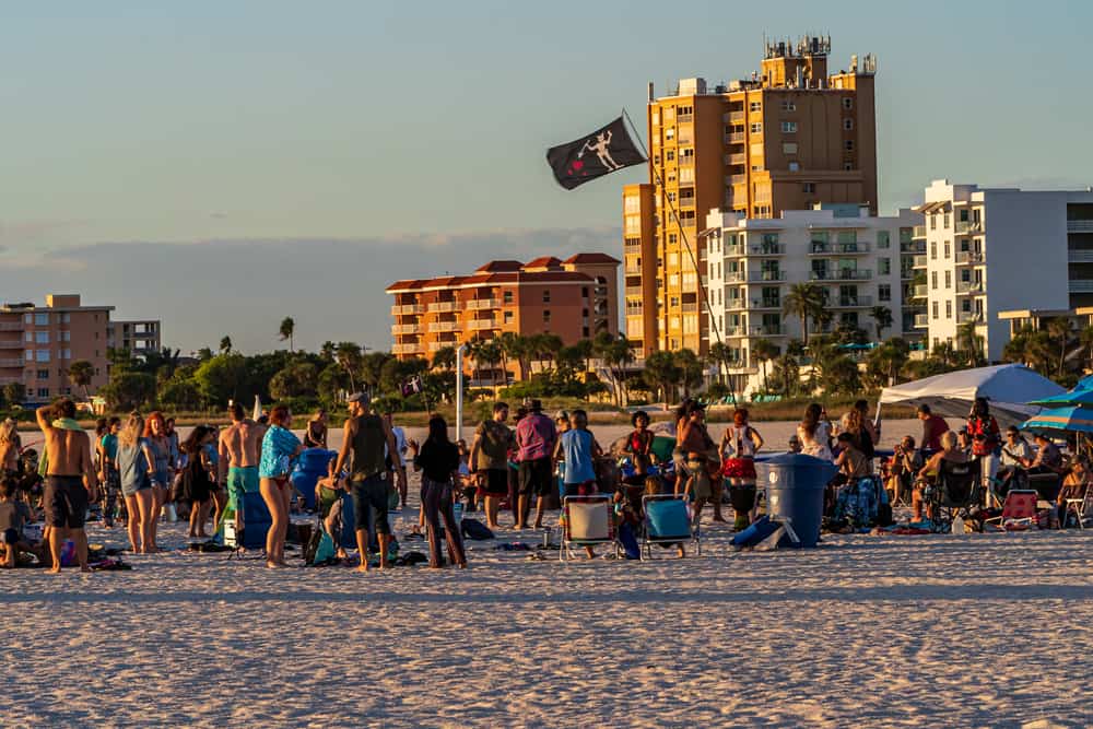 A crowd of people stand while others play on the beach during the sunset drum circle, one of the best things to do in Treasure Island.