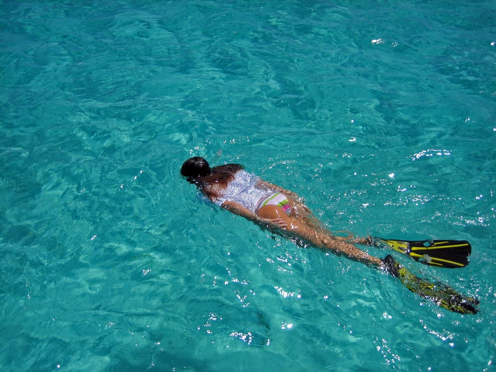 A young girl floats atop the bright blue water, witnessing the best snorkeling in the Florida Keys through her fins, mask, and admiration. 
