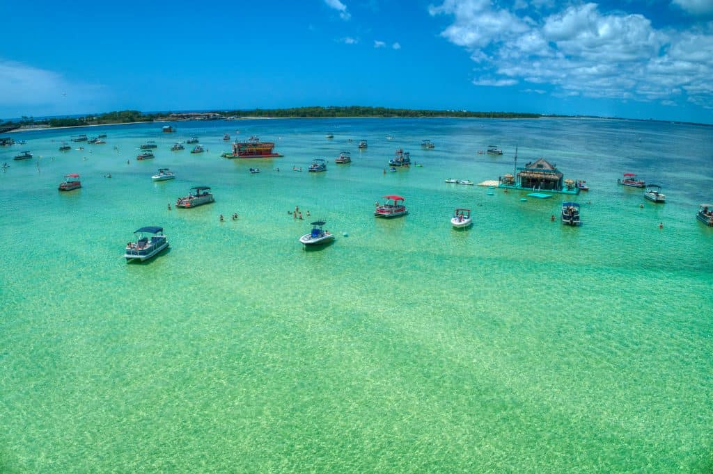 Dozens of motor boats sit moored on the sand bar of Crab Island, where people swim in the bright blue green water.