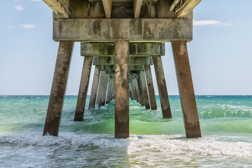 Bright green waves crash under the wooden beams of the pier at Okaloosa Island, which has some of the best beaches near Destin.