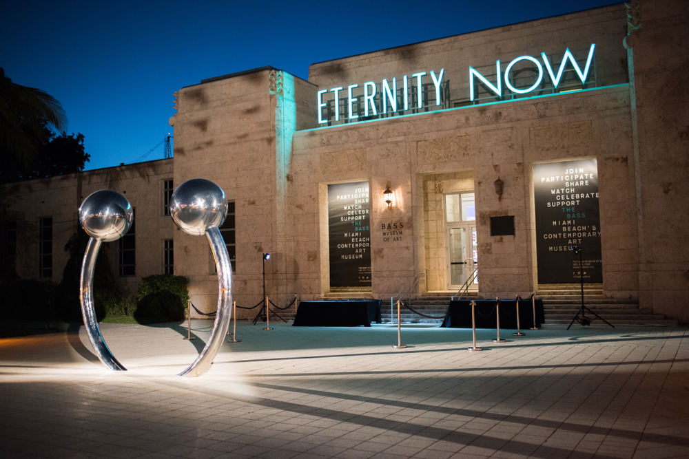 Nighttime exterior of the museum with a metal sculpture and neon sign reading "Eternity Now"