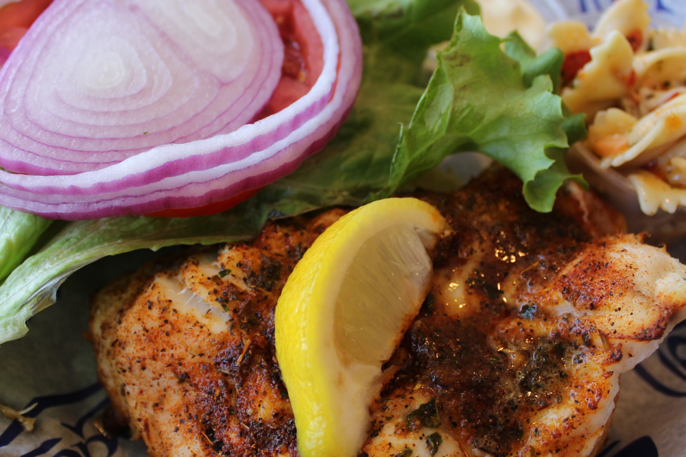 A closeup of a blackened grouper sandwich, with lettuce, onion, and a wedge of lemon. Grouper is one of the most popular meals at Keegan's Seafood Grille in Indian Rocks Beach.