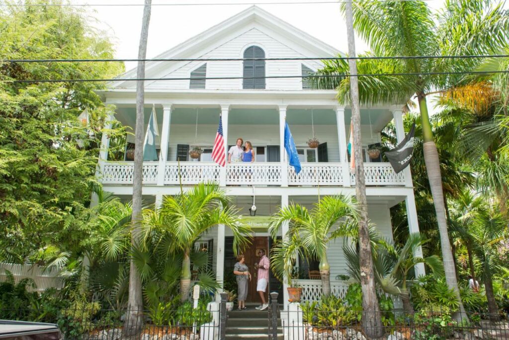 A shot of the exterior of the Old Town Manor, lots of palm trees surround the building and contrast the stark white of its paint. It's where to stay in Key West if you're looking for a great time! 