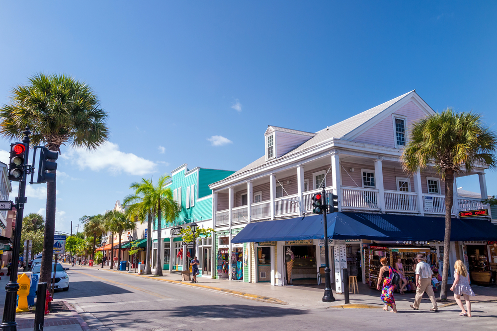 a daytime shot of the historic old town in Key west, there are lots of colorful storefronts and palm trees lining the street 
