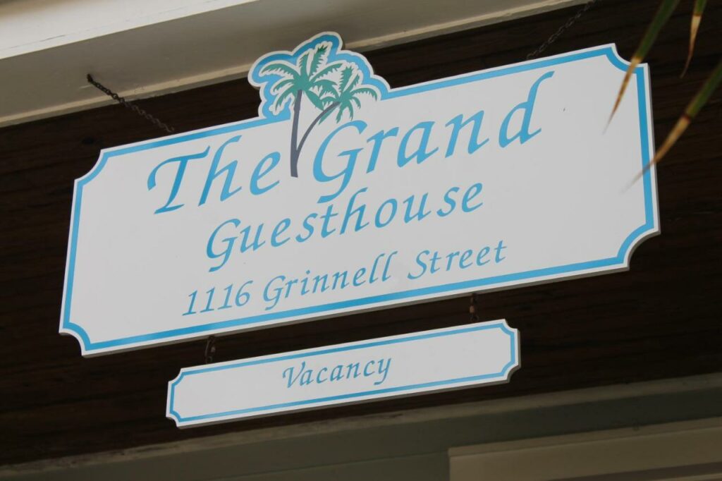A picture of the sign of the Grand Guesthouse in Key West, the sign features a logo of a palm tree in the center 